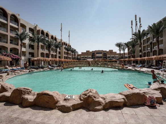 Luxury swimming pool at AlKarma Aqua Beach surrounded by palm trees and modern resort-style architecture.