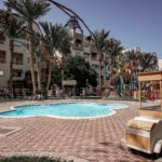 Luxury swimming pool at AlKarma Aqua Beach surrounded by palm trees and modern resort-style architecture.