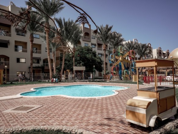Luxury swimming pool at AlKarma Aqua Beach surrounded by palm trees and modern resort-style architecture.