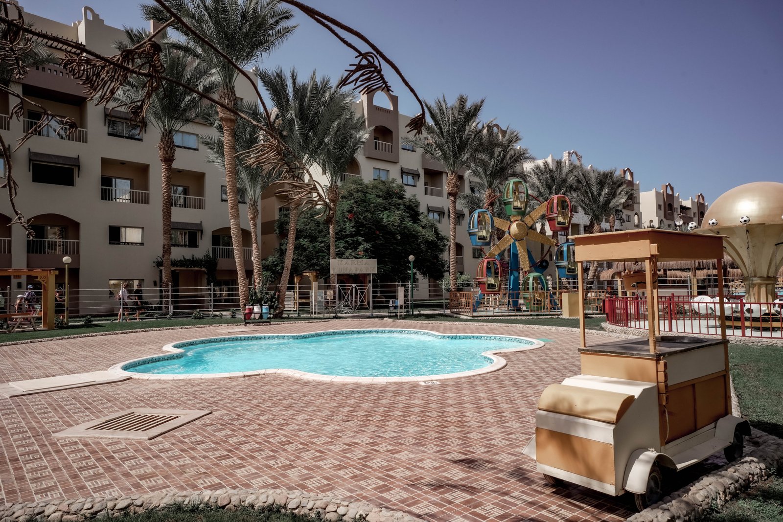 Luxury swimming pool at AlKarma Aqua Beach surrounded by palm trees and modern resort-style architecture.