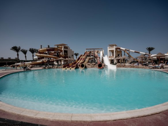 Luxury swimming pool at AlKarma Aqua Beach surrounded by palm trees and modern resort-style architecture.