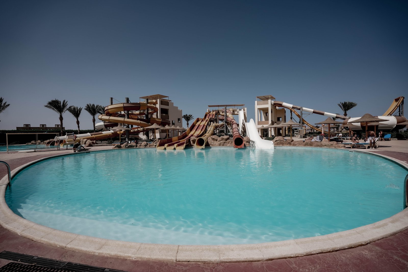 Luxury swimming pool at AlKarma Aqua Beach surrounded by palm trees and modern resort-style architecture.
