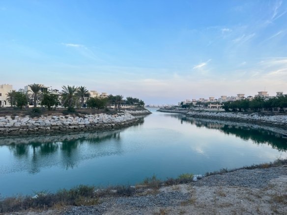 Pedestrian street scene in Kafr El Gouna featuring dome-roofed Nubian architecture, pastel-colored buildings, boutique shops, and vibrant outdoor cafes bordering a calm lagoon.